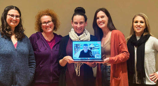 Five SANDSWA members pose with a computer, featuring a Zoom call with author Carl Zimmer